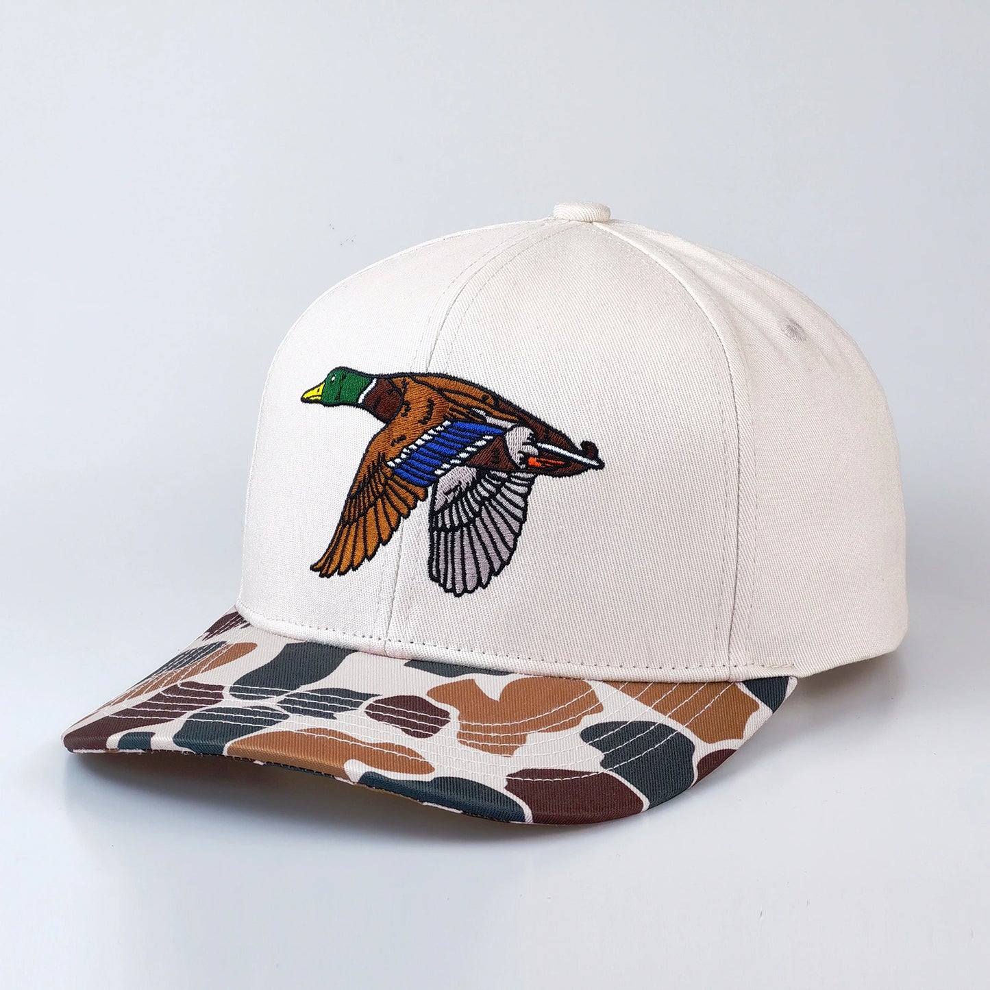 Off white cap with a colorful duck design on the front and camouflage-patterned brim on a light gray background